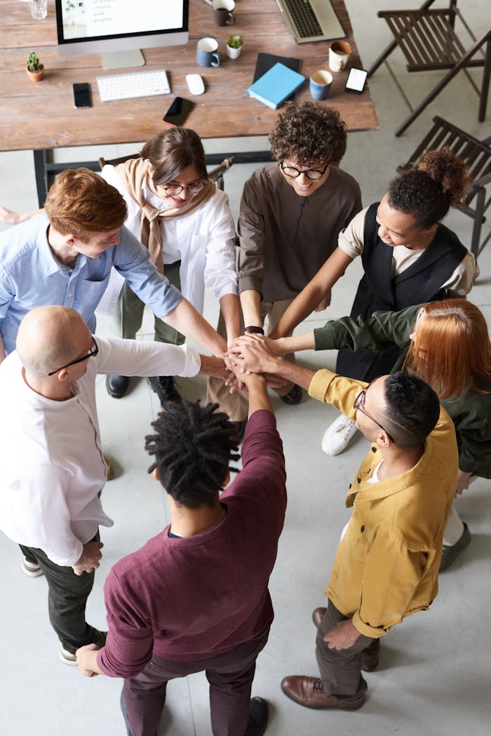 about-me A diverse group of professionals joins hands in a team-building exercise indoors.