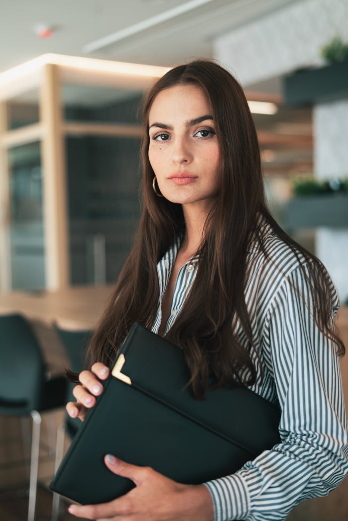 my-work-01 Portrait of a confident businesswoman with long hair holding documents in a modern office setting.