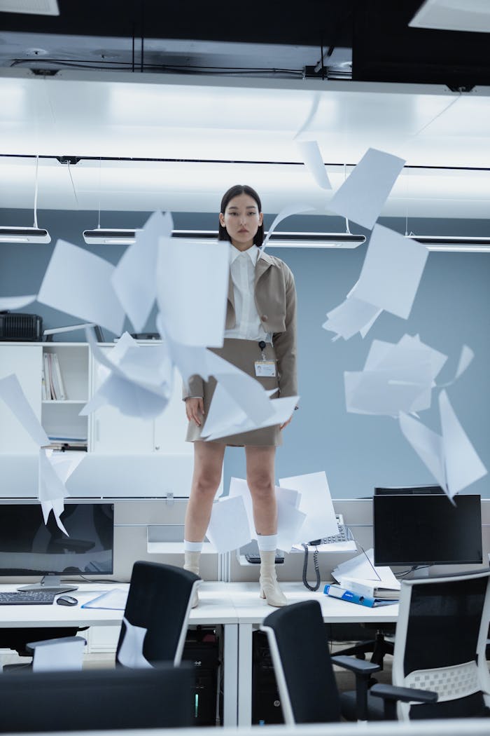 photography-service-02 A woman in a modern office with papers flying around, capturing a dynamic and energetic moment.