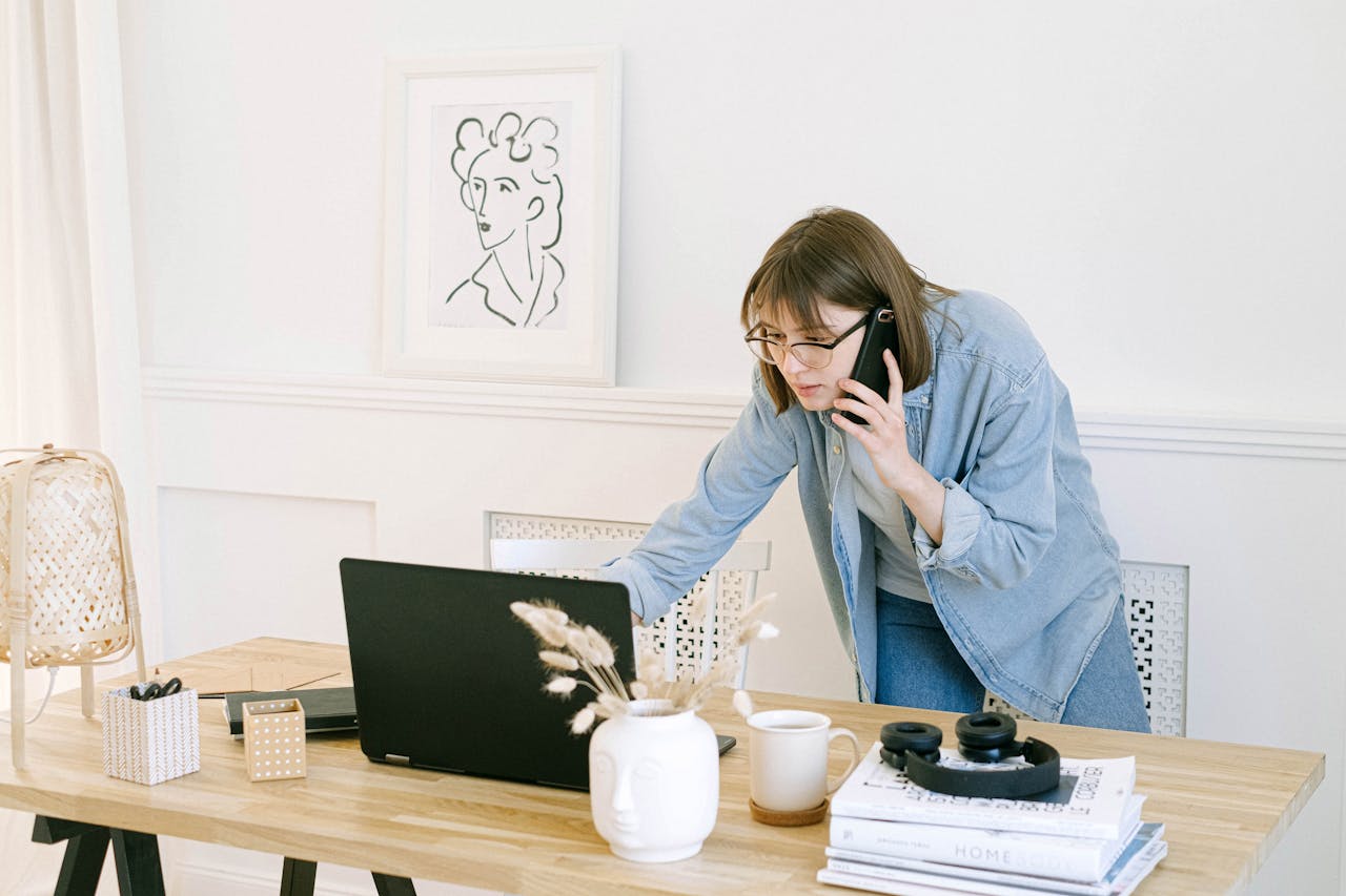 contact-img Woman multitasking with laptop and phone in modern home office setting.